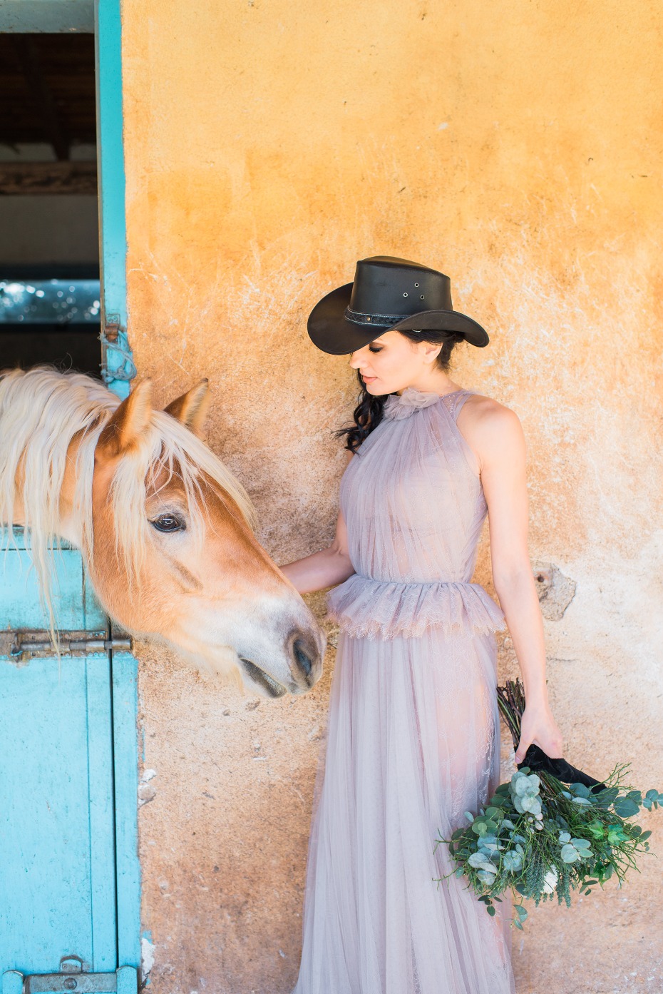 Cowgirl in tulle dress strokes blonde horse in stable