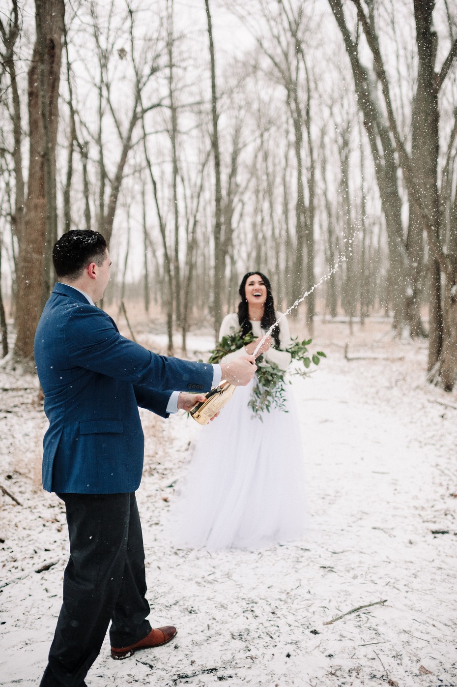 Groom pops champagne with bride on their winter wedding day