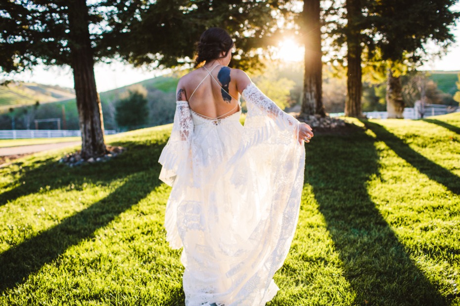 Bride in white dress with bird tattoo walks through field