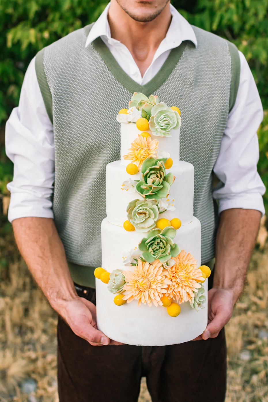 Man holding a tiered wedding cake with flower decor