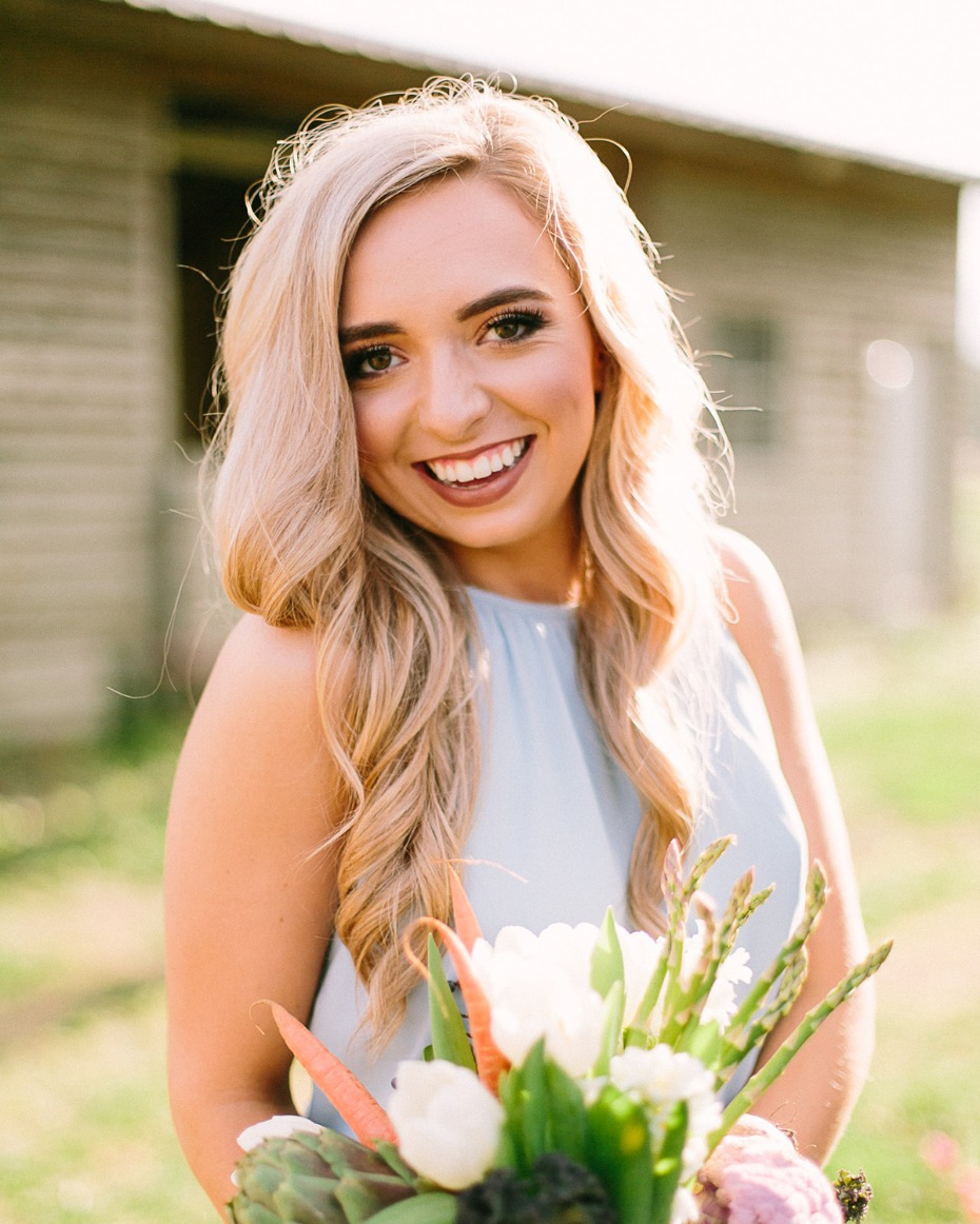 Blonde woman smiles holding flower and vegetable bouquet