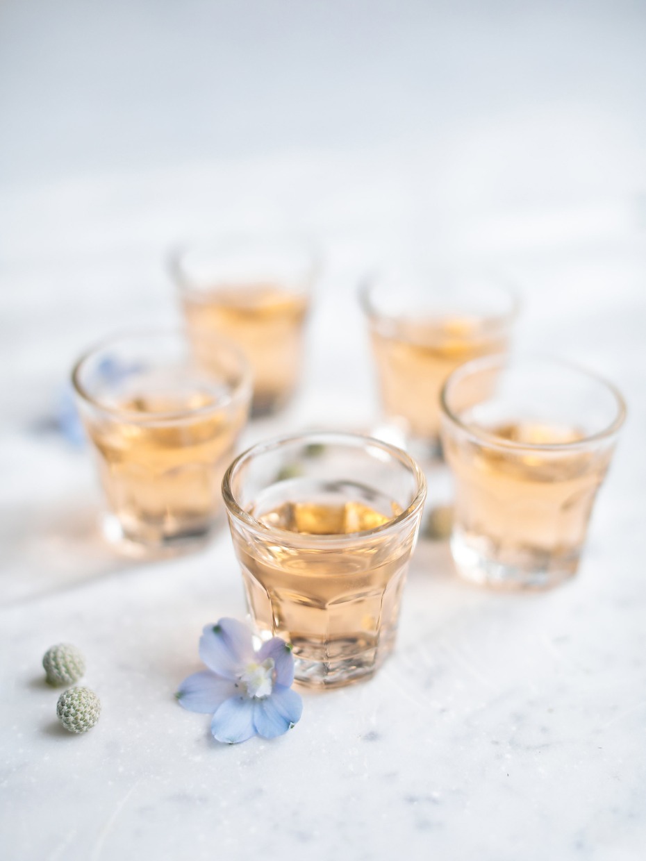 Five shot glasses of rose-colored drink with flower garnishes