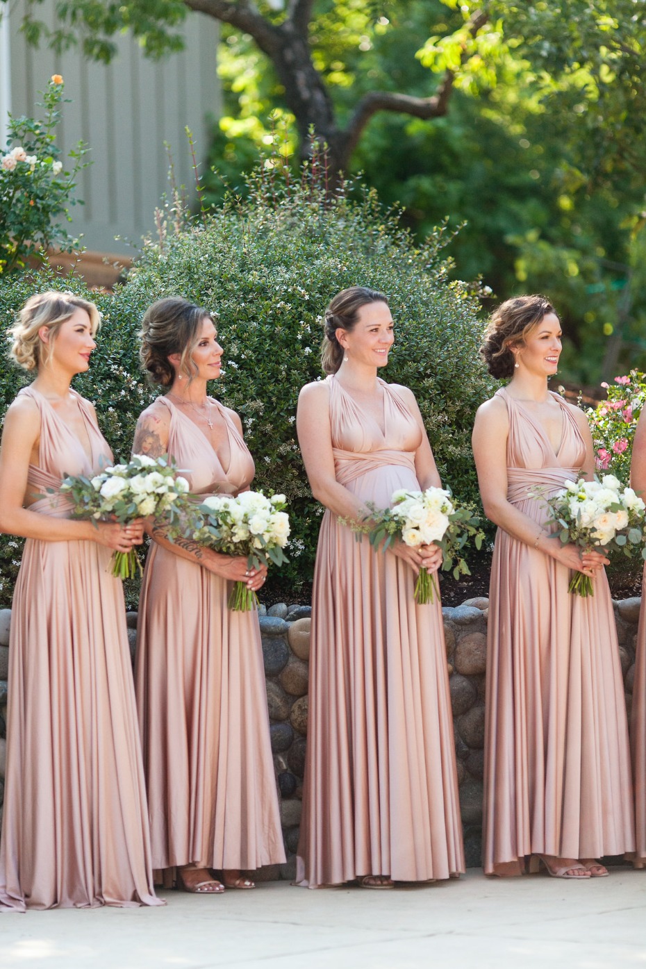 Bridesmaids in blush dresses holding bouquets outdoors