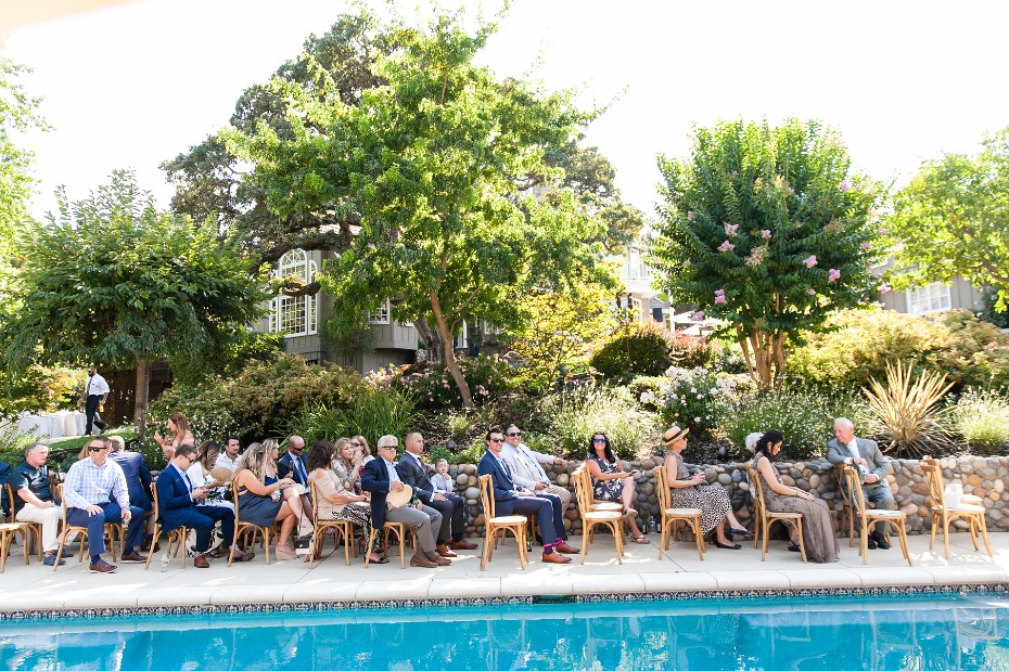 Wedding guests seated poolside in a lush garden setting