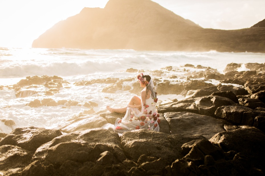Bride in floral dress on rocky beach coastline at sunset