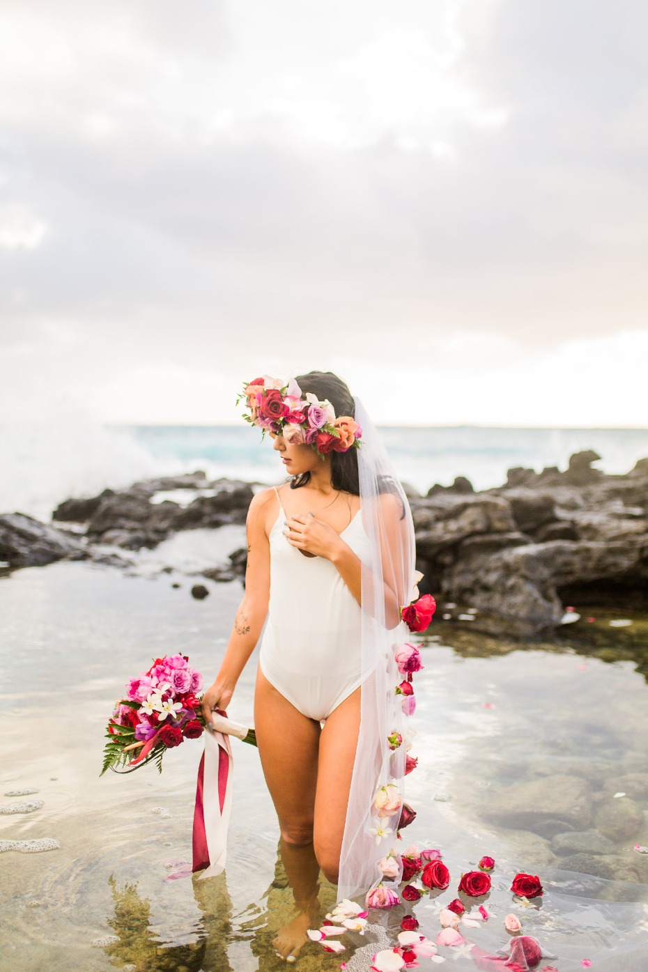 Beach bride in floral veil and swimsuit holding bouquet