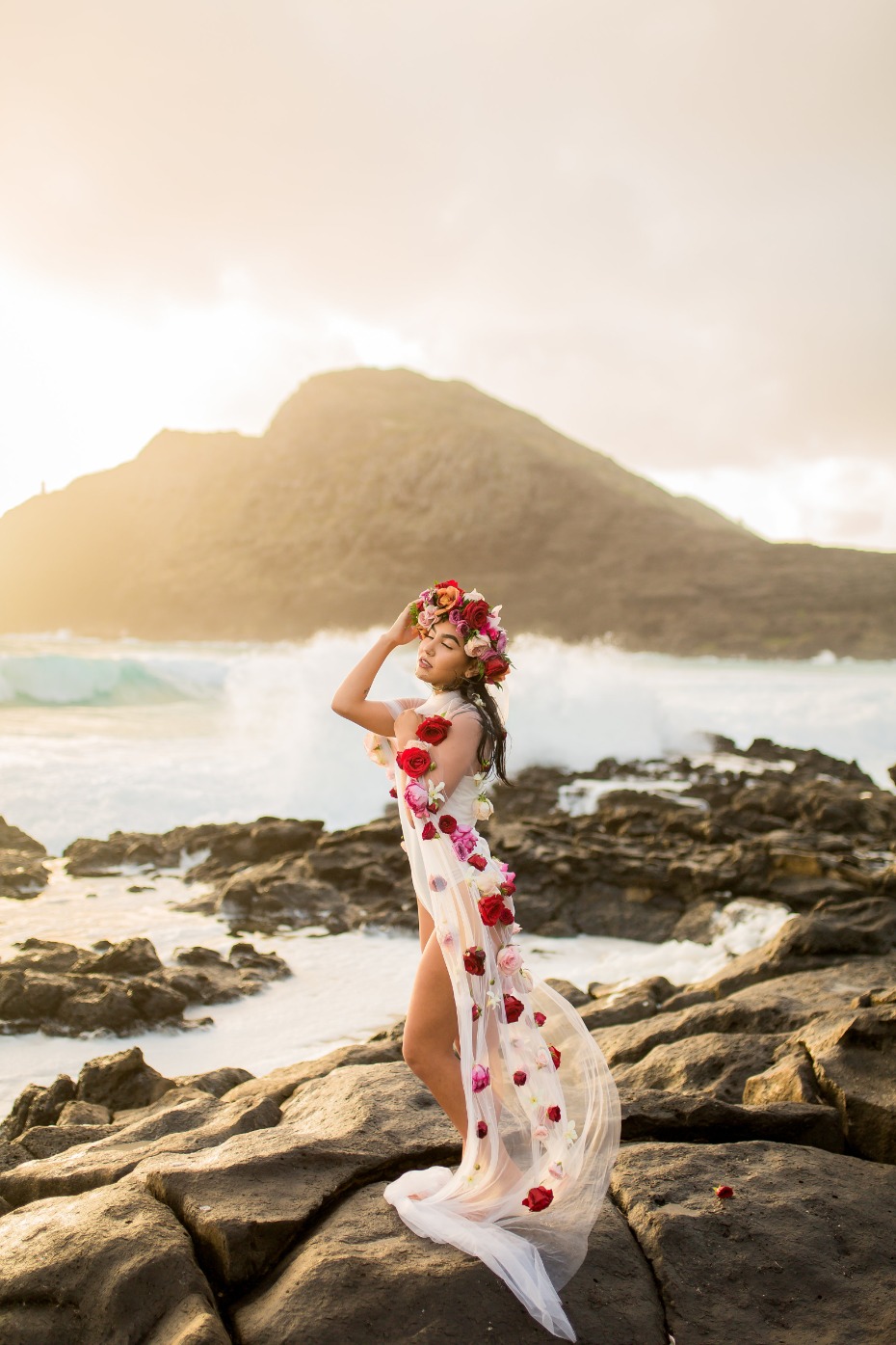 Woman in floral dress poses on rocks by ocean shore
