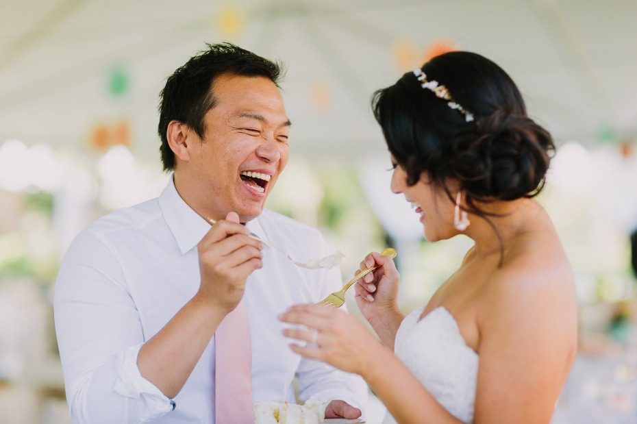 Bride and groom laughing while feeding each other cake at wedding