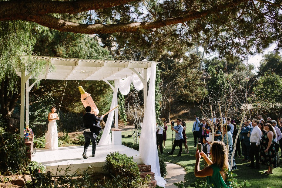 Bride and groom playing piñata during a festive outdoor wedding party