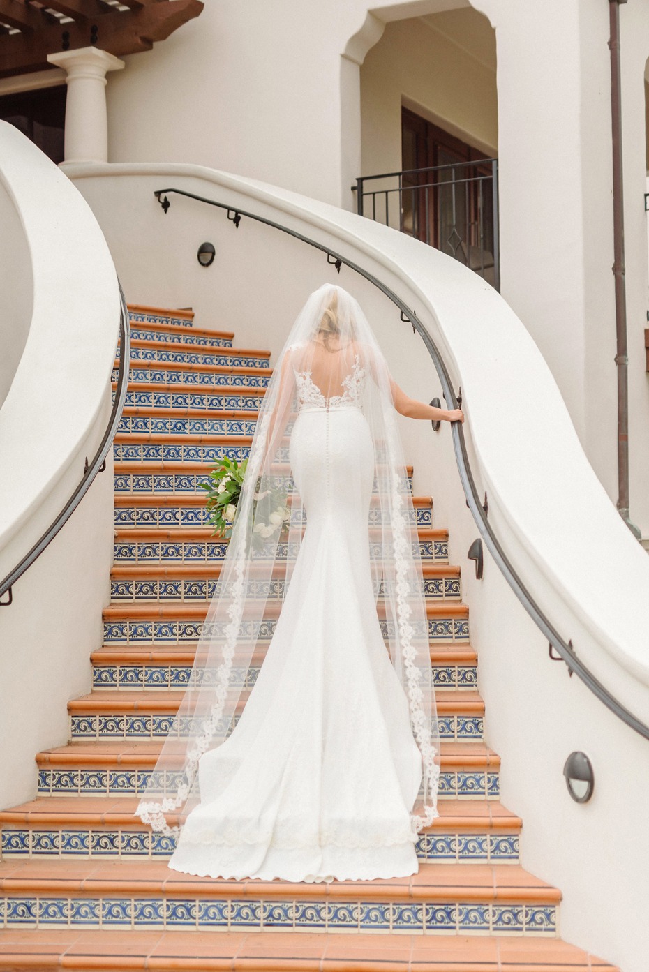 Bride in white wedding dress ascends stairs with veil trailing