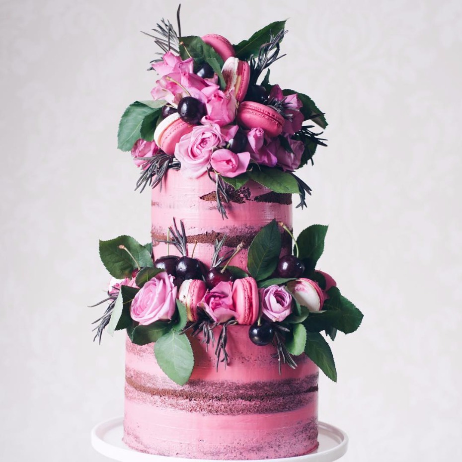 Two-tiered pink cake with macarons cherries and flowers