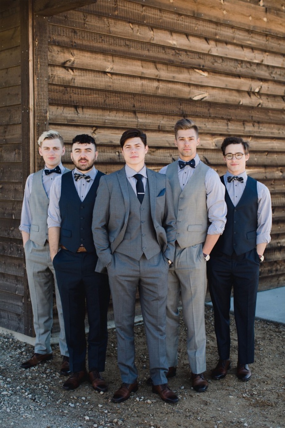 Groomsmen in stylish suits before a rustic wedding barn
