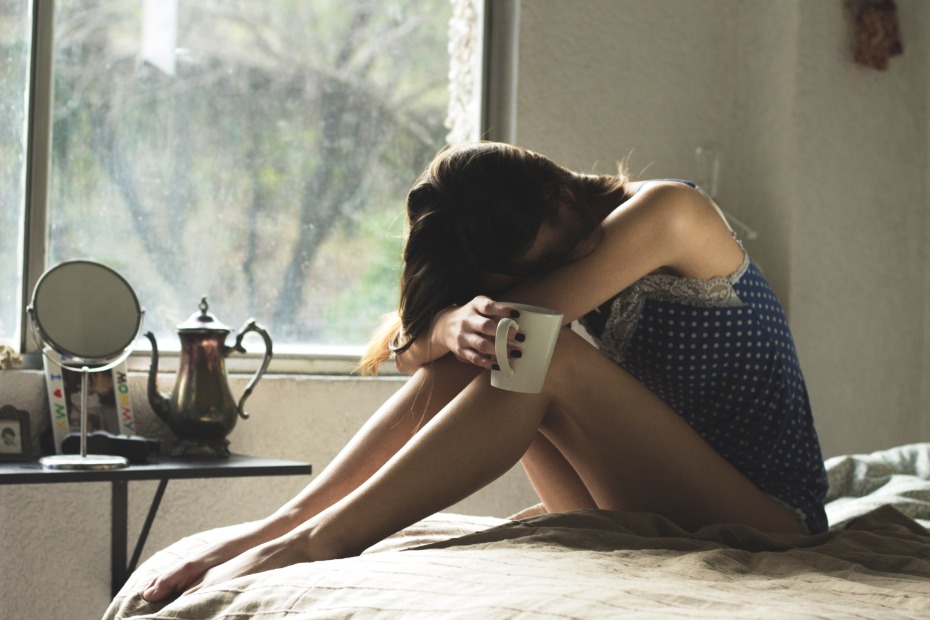 Woman embraces knees holding mug in somber morning light