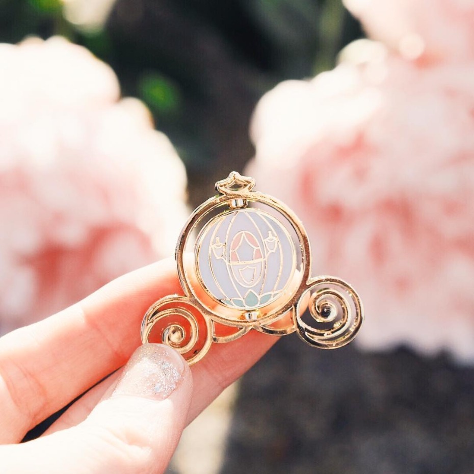 Hand holds a golden Cinderella pumpkin carriage pin