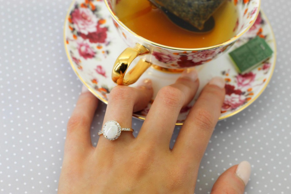Engagement ring on hand with tea in floral cup nearby