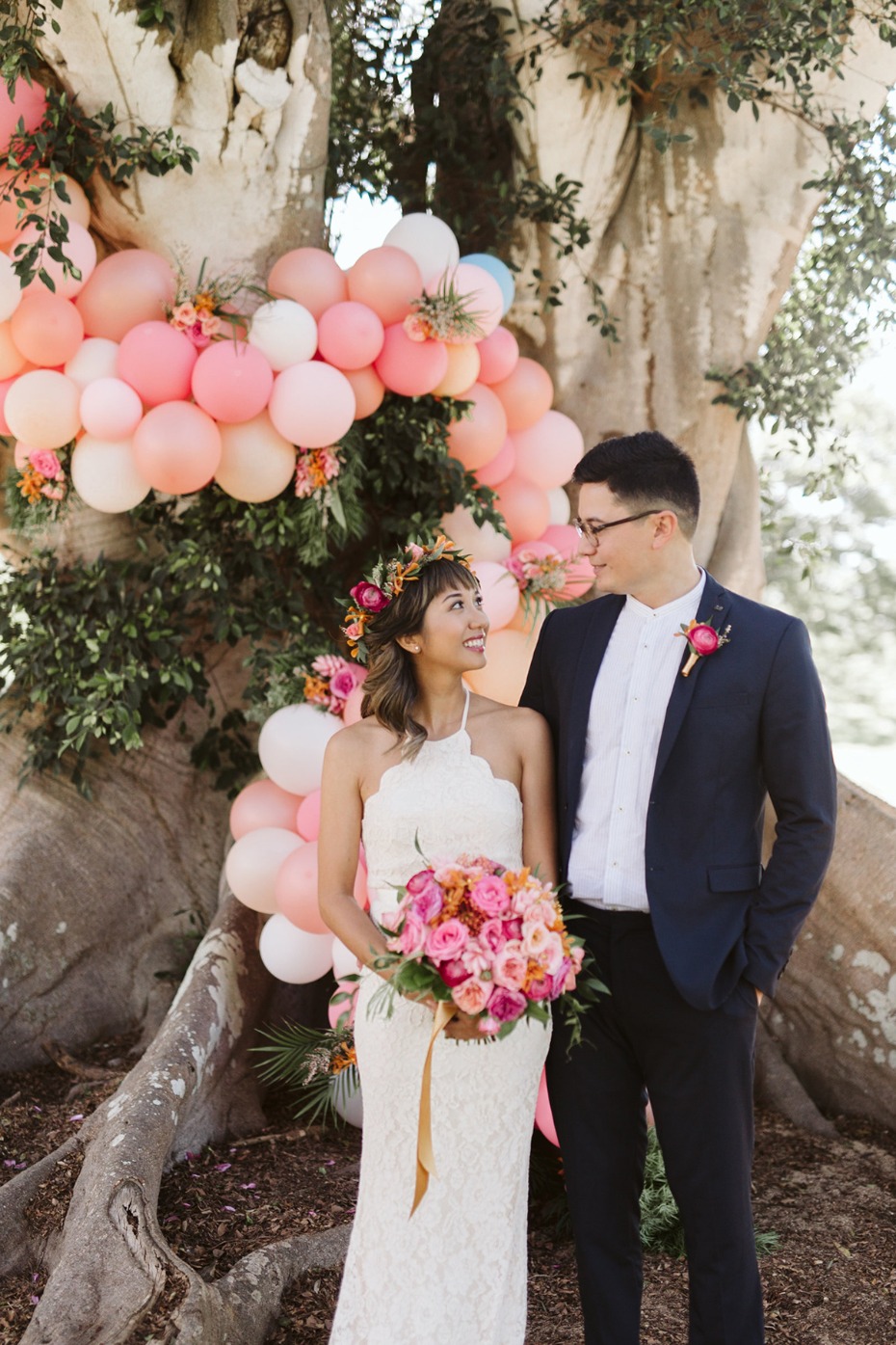 Happy couple smiles at wedding with balloon arch and flowers