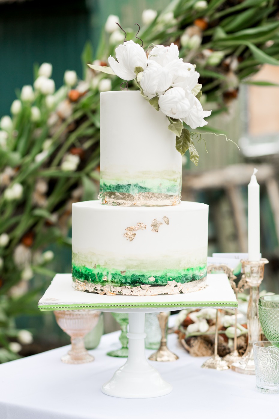 Elegant two-tiered wedding cake with green and gold accents, flowers