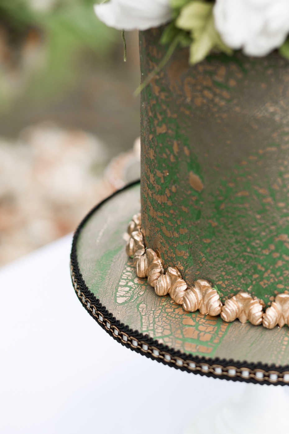 Elegant green and gold cake with floral arrangement on a white table