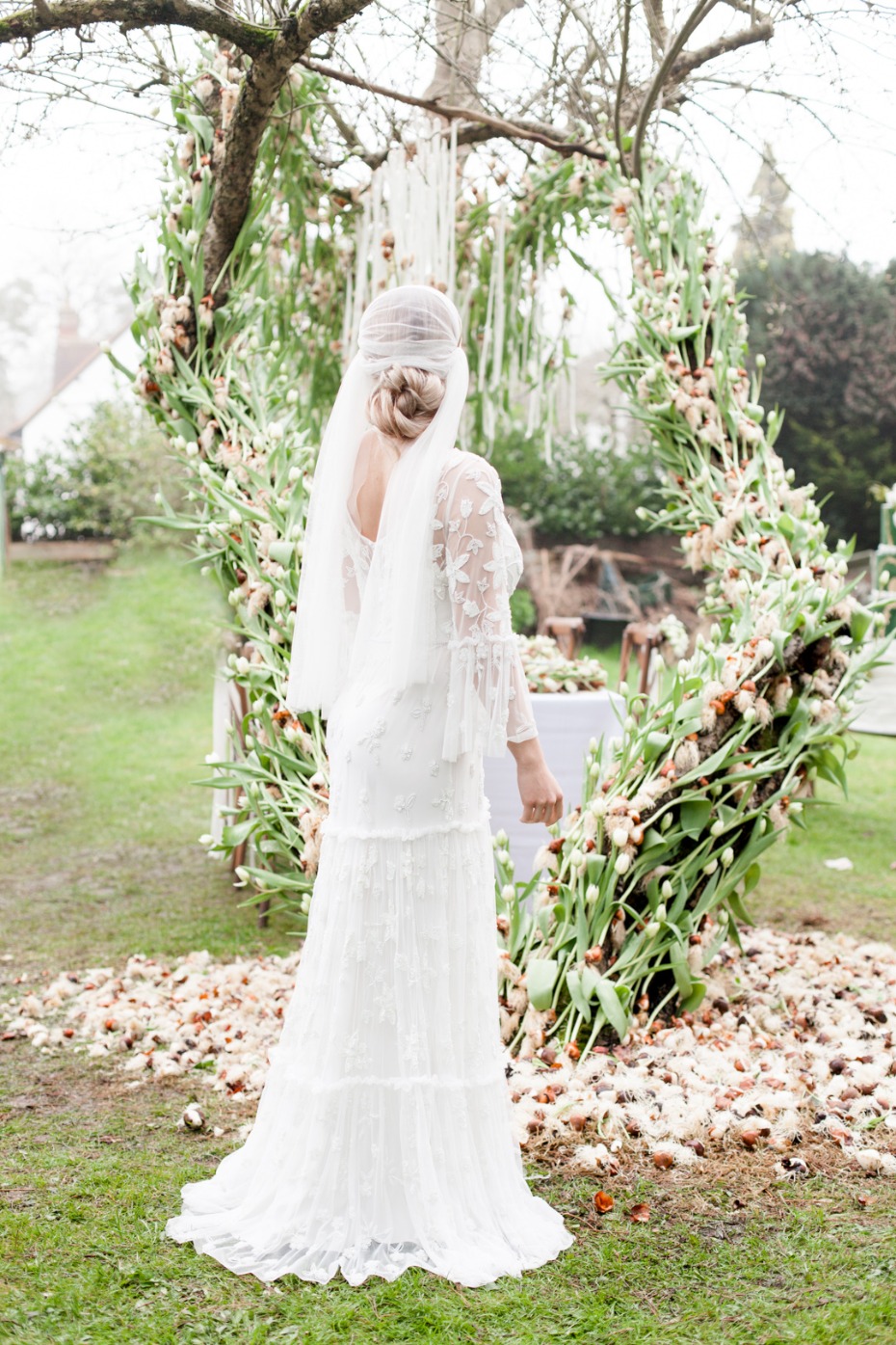 Bride in beautiful wedding dress poses before floral archway