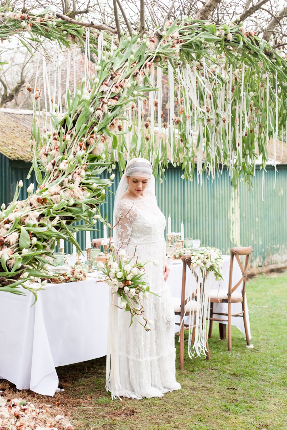 Bride in elegant lace gown under a flower arch at outdoor wedding