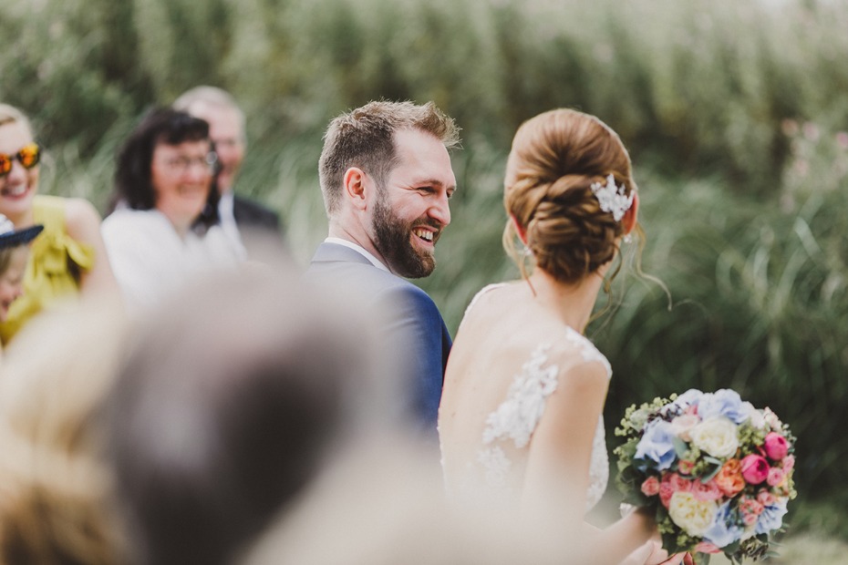 Happy groom smiles at his bride during an outdoor wedding ceremony