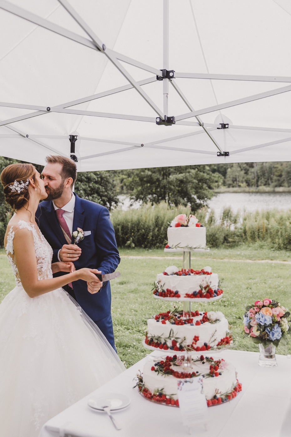 Bride and groom kissing as they cut their tiered wedding cake