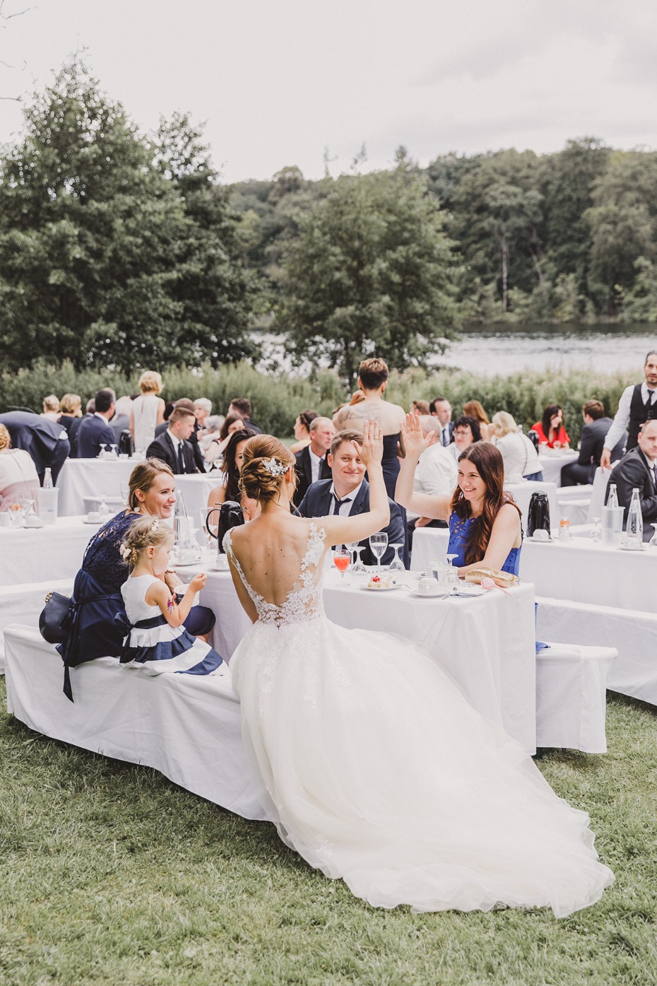 Bride waves from wedding table, celebrating with guests, outdoor reception