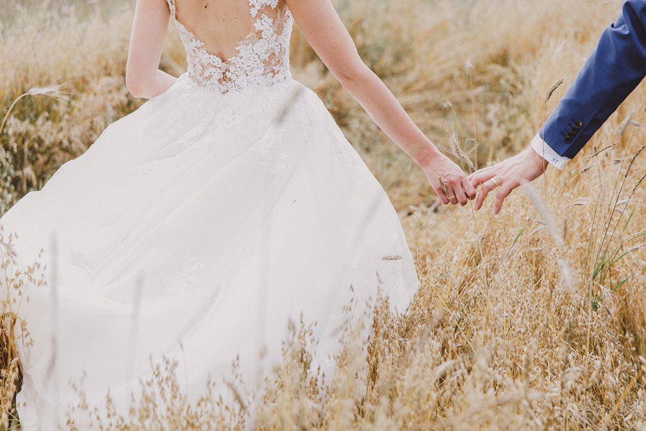 Bride and groom holding hands in a golden field during their wedding day