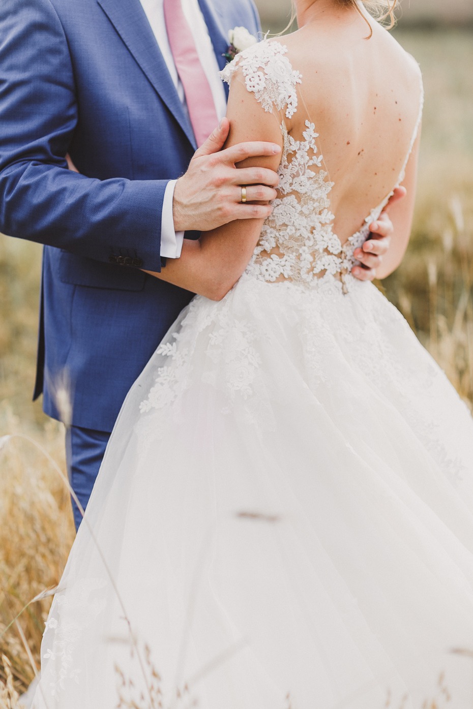 Bride and groom embracing, wedding dress details visible close up