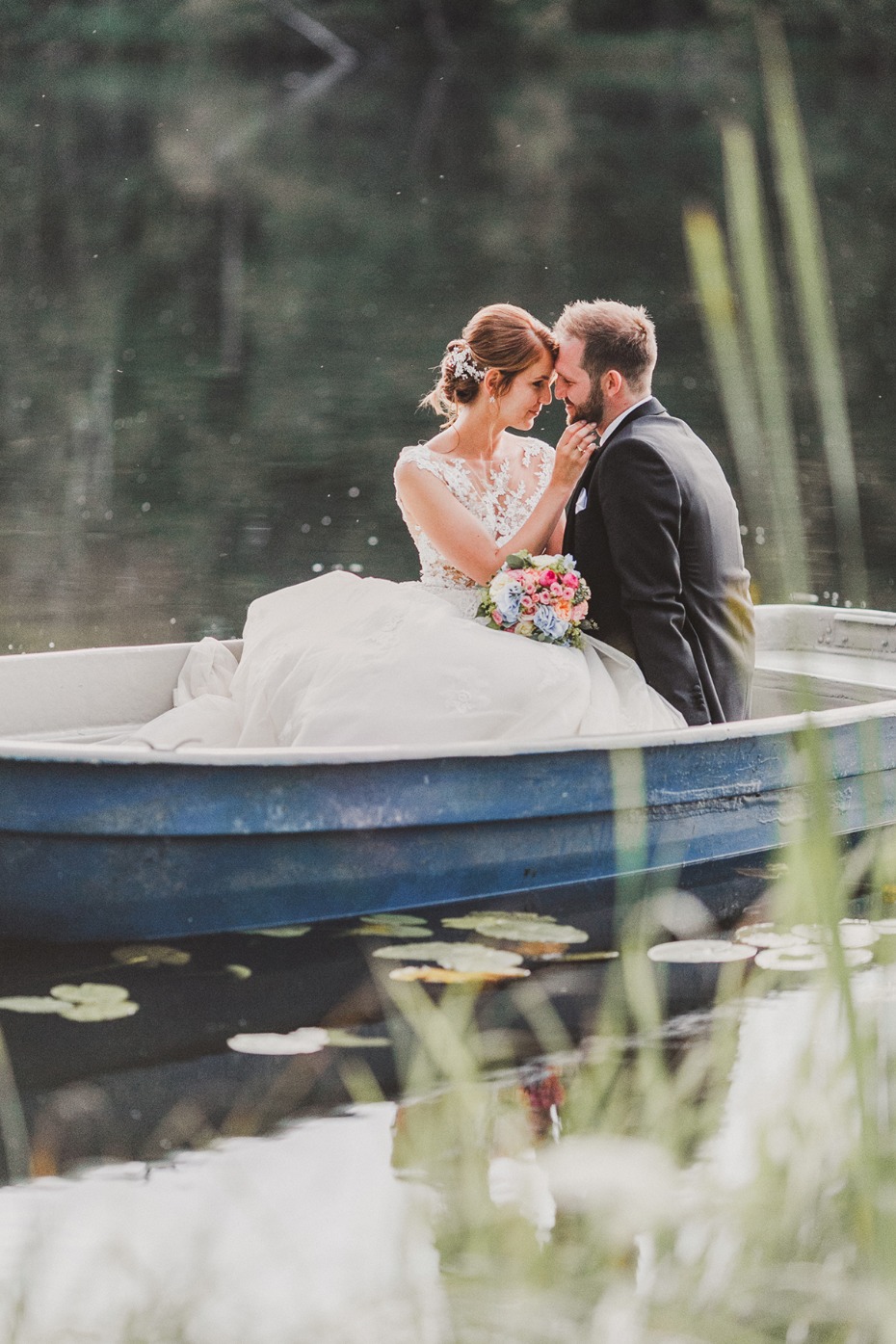 Bride and groom in boat at lake on wedding day romantic pose