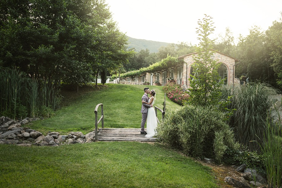 Bride and groom kiss on a bridge in lush landscape