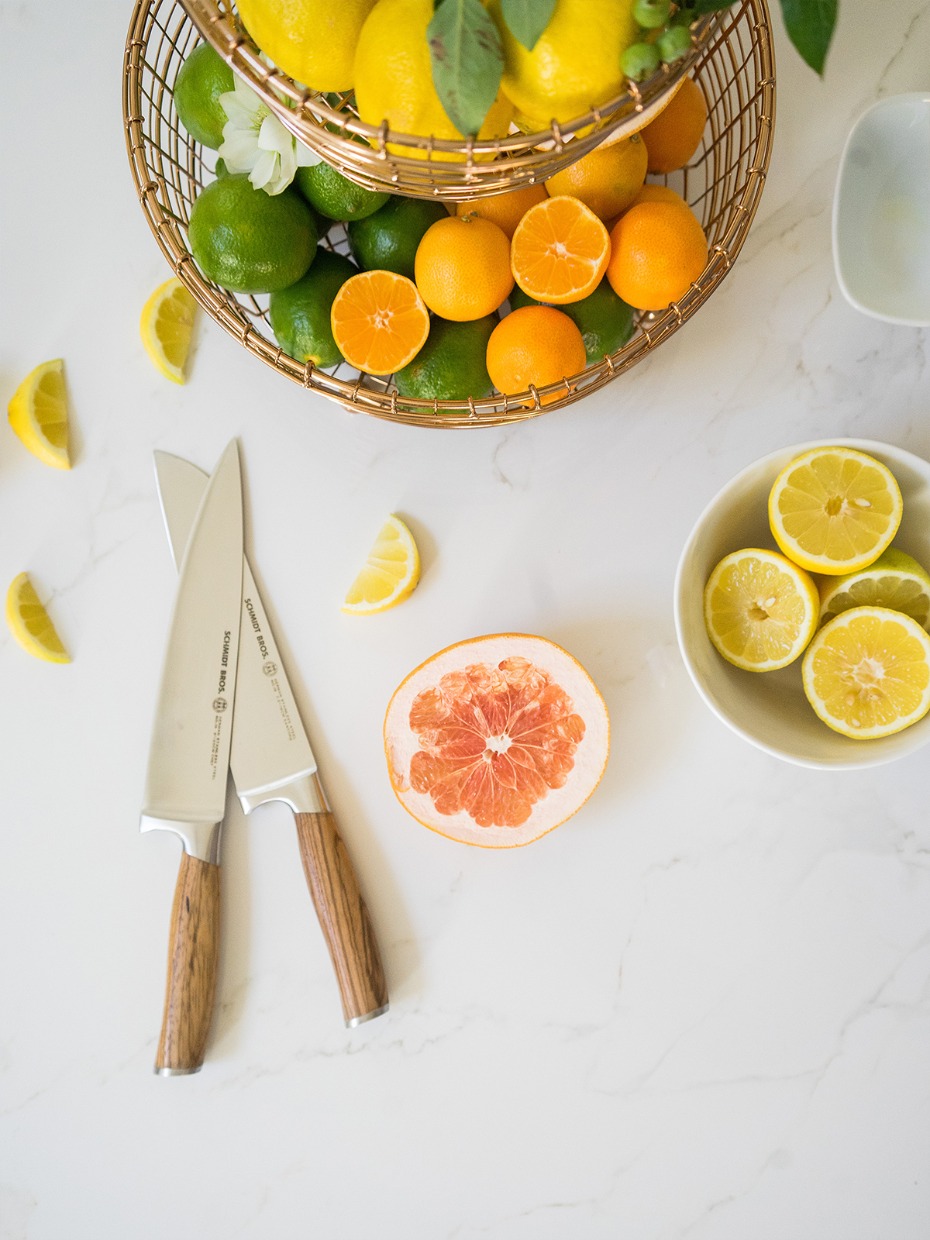 Fresh citrus fruits, knives, and a grapefruit arranged on a counter