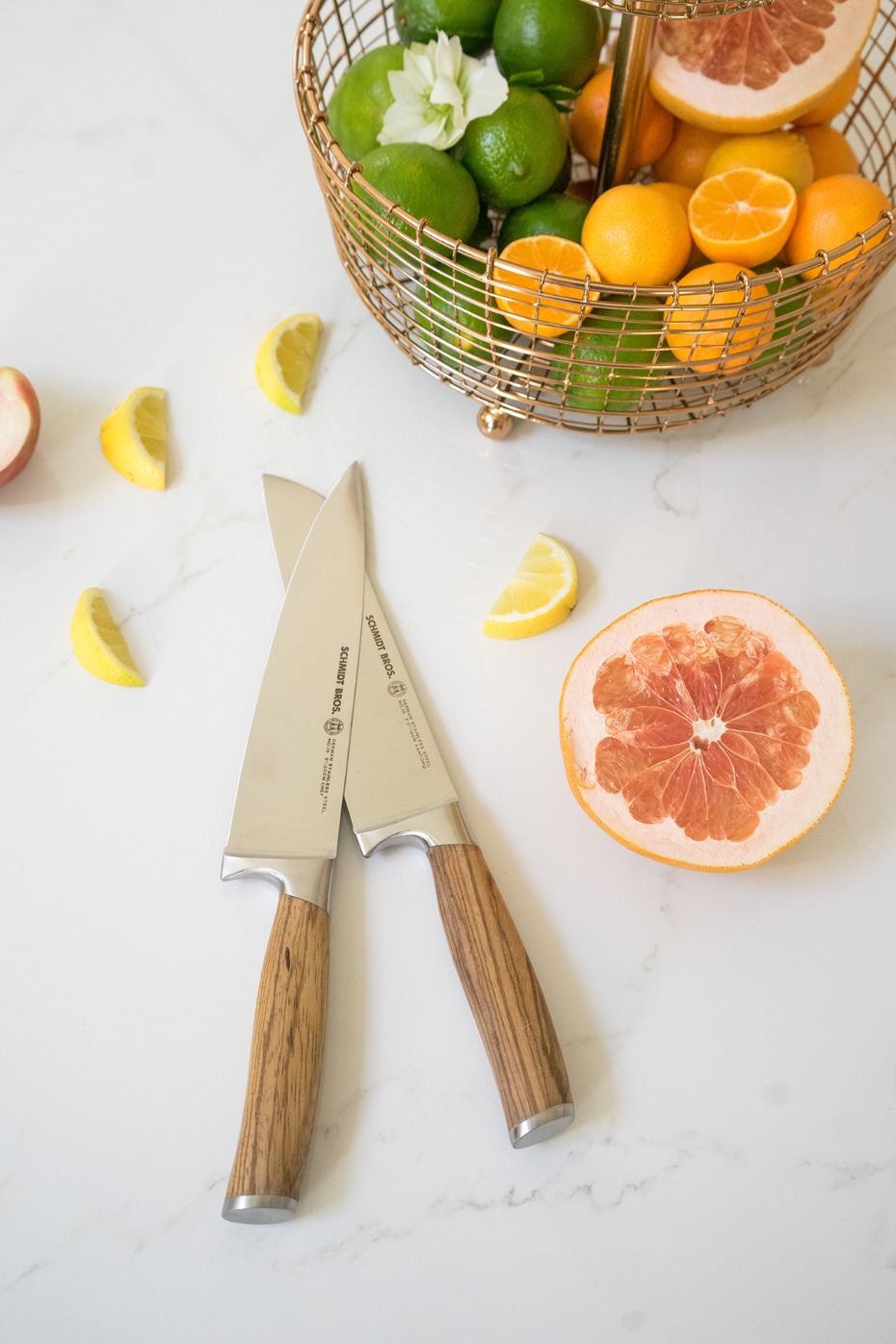 Two kitchen knives with fruit and a fruit basket on a counter