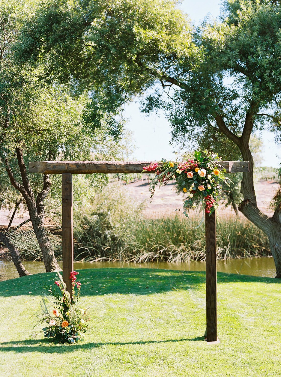 Rustic wood wedding arch decorated with flowers by pond