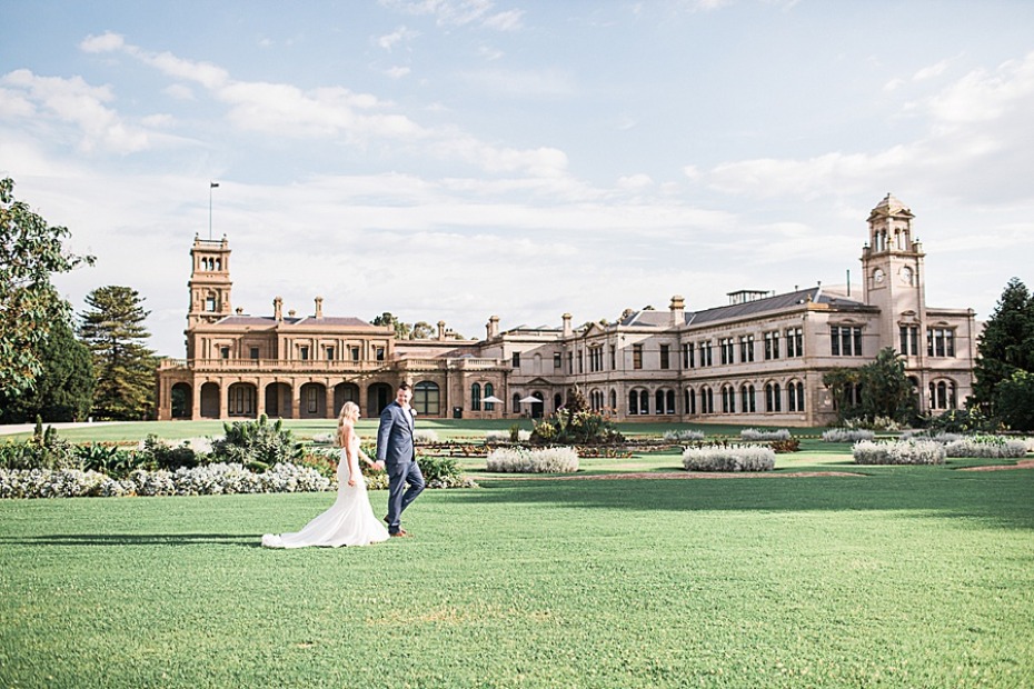 Bride and groom walk on grass towards a beautiful building