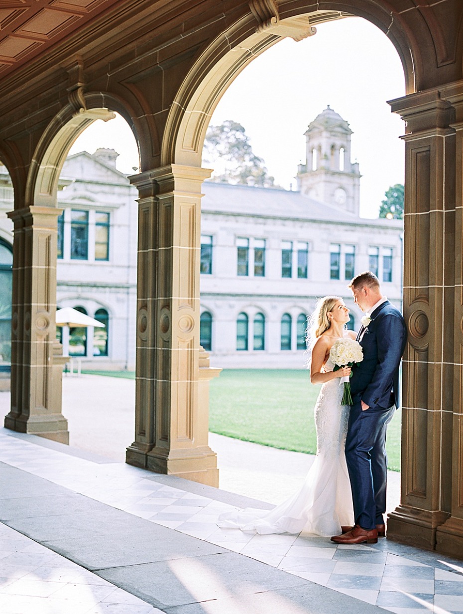 Elegant wedding couple posing under archway of a grand building