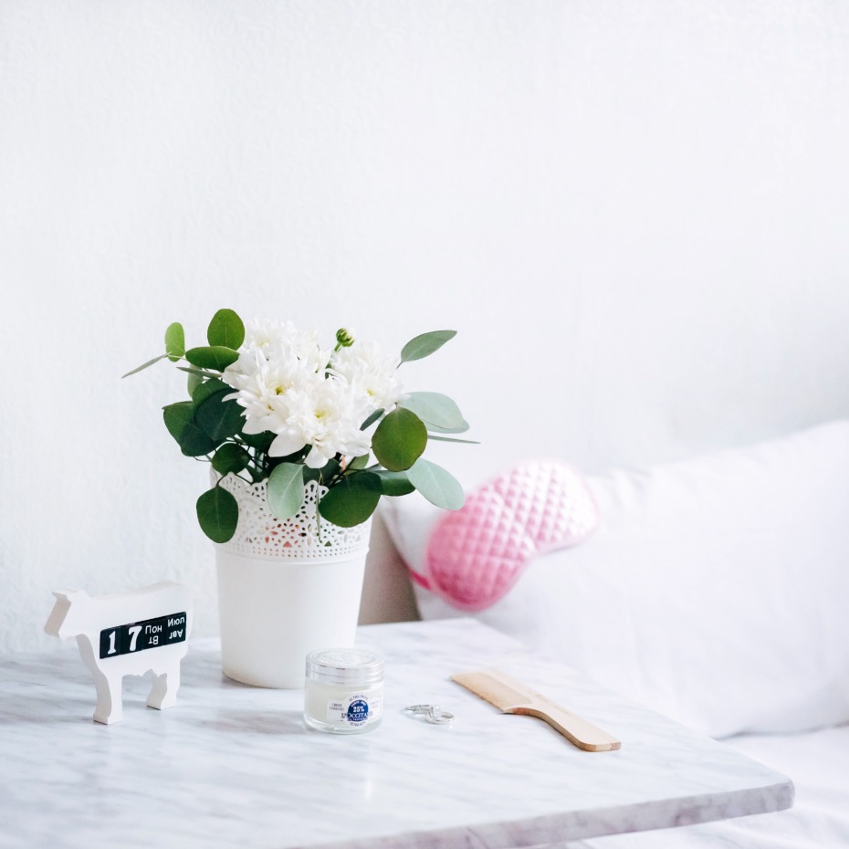 White flowers and skincare on a marble bedside table