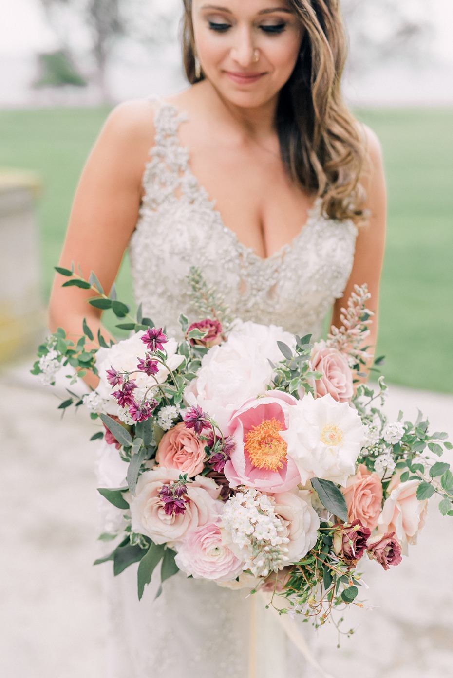 Bride in embellished dress holds pastel flower bouquet
