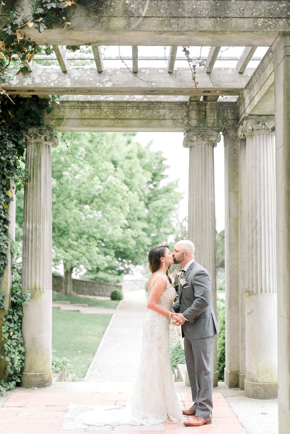 A couple kissing during their wedding ceremony under a pergola