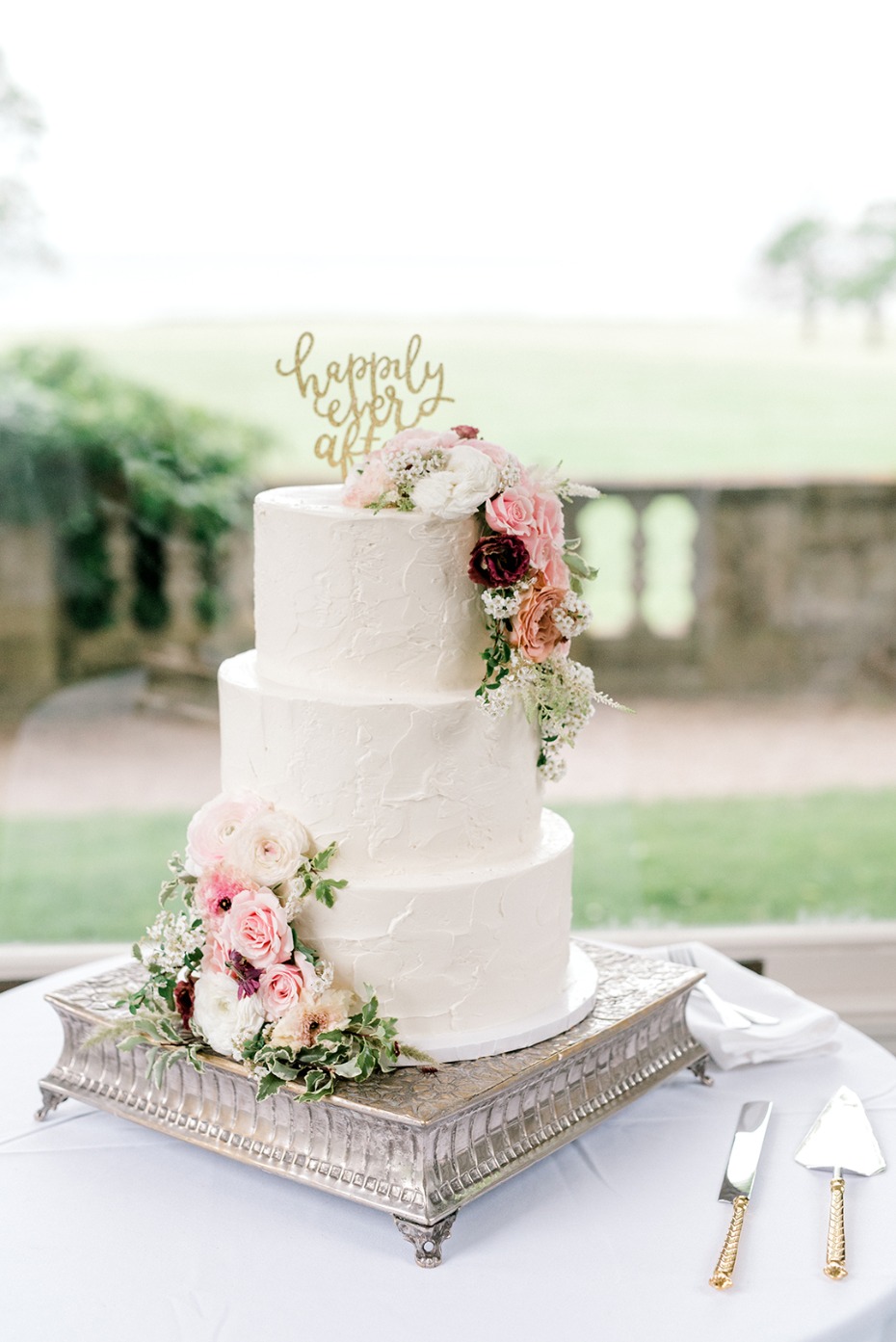 Elegant three-tiered wedding cake with floral accents and Happily Ever After topper