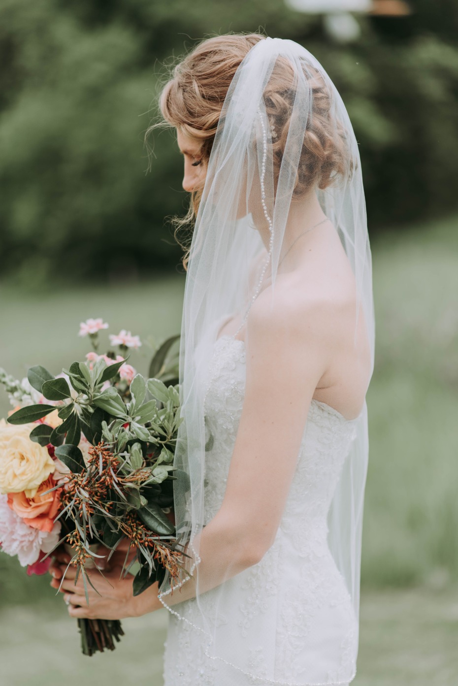 Bride looking down at her bouquet with veil on