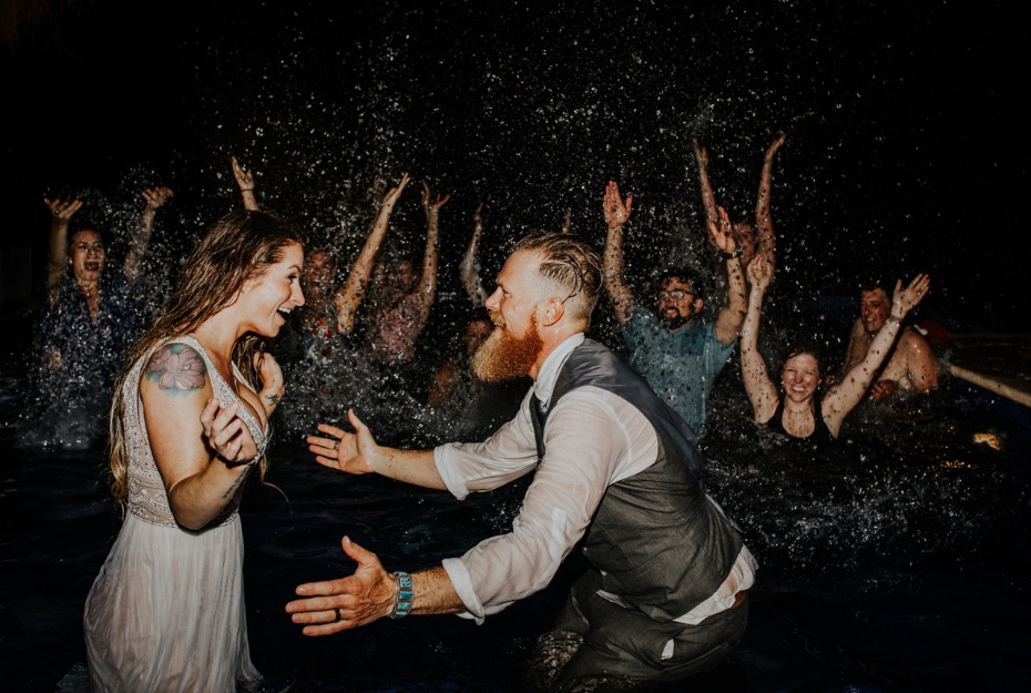 Bride and groom splashing in the water with their wedding party