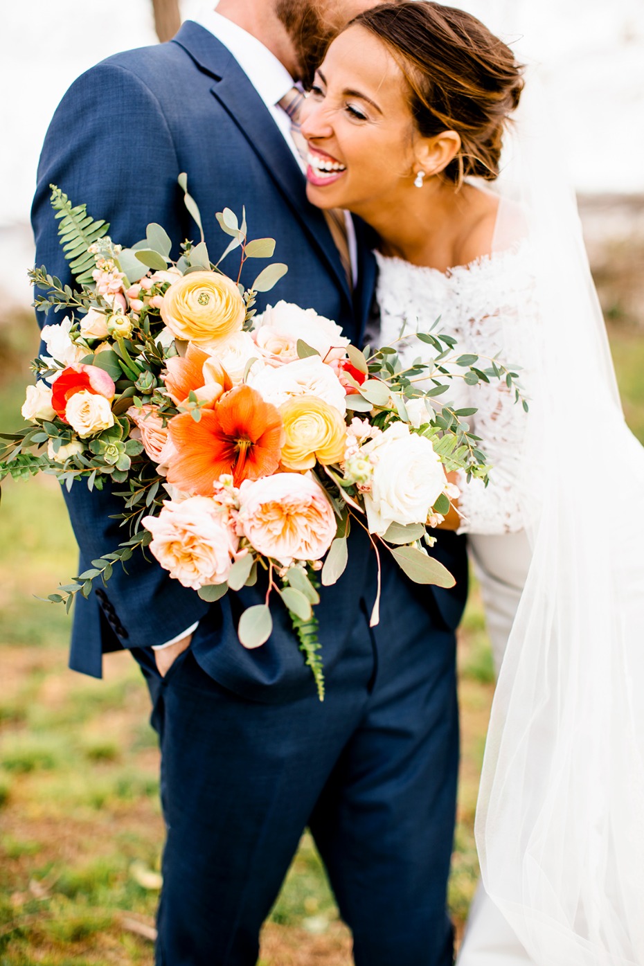 Happy bride smiles with wedding bouquet, groom in blue suit