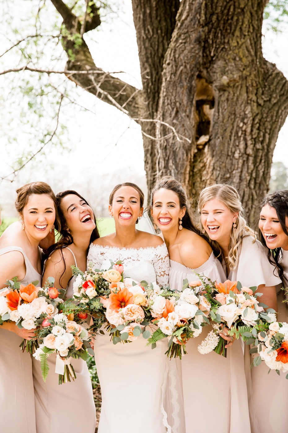 Bride and bridesmaids laughing on wedding day with bouquets