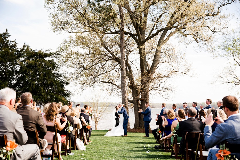 Outdoor wedding ceremony with a kissing couple and guests