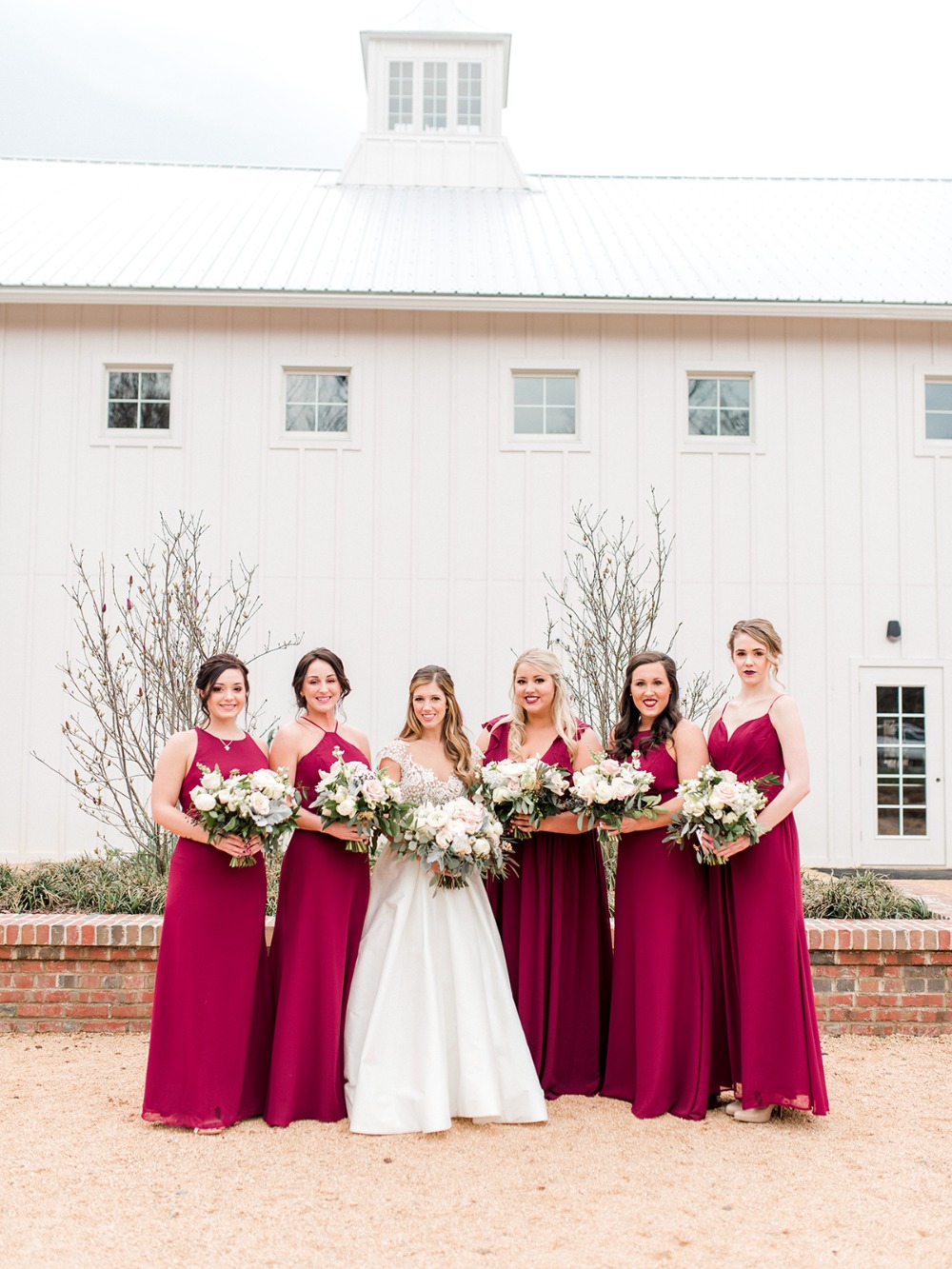 Bride with bridesmaids in burgundy dresses in front of a white building