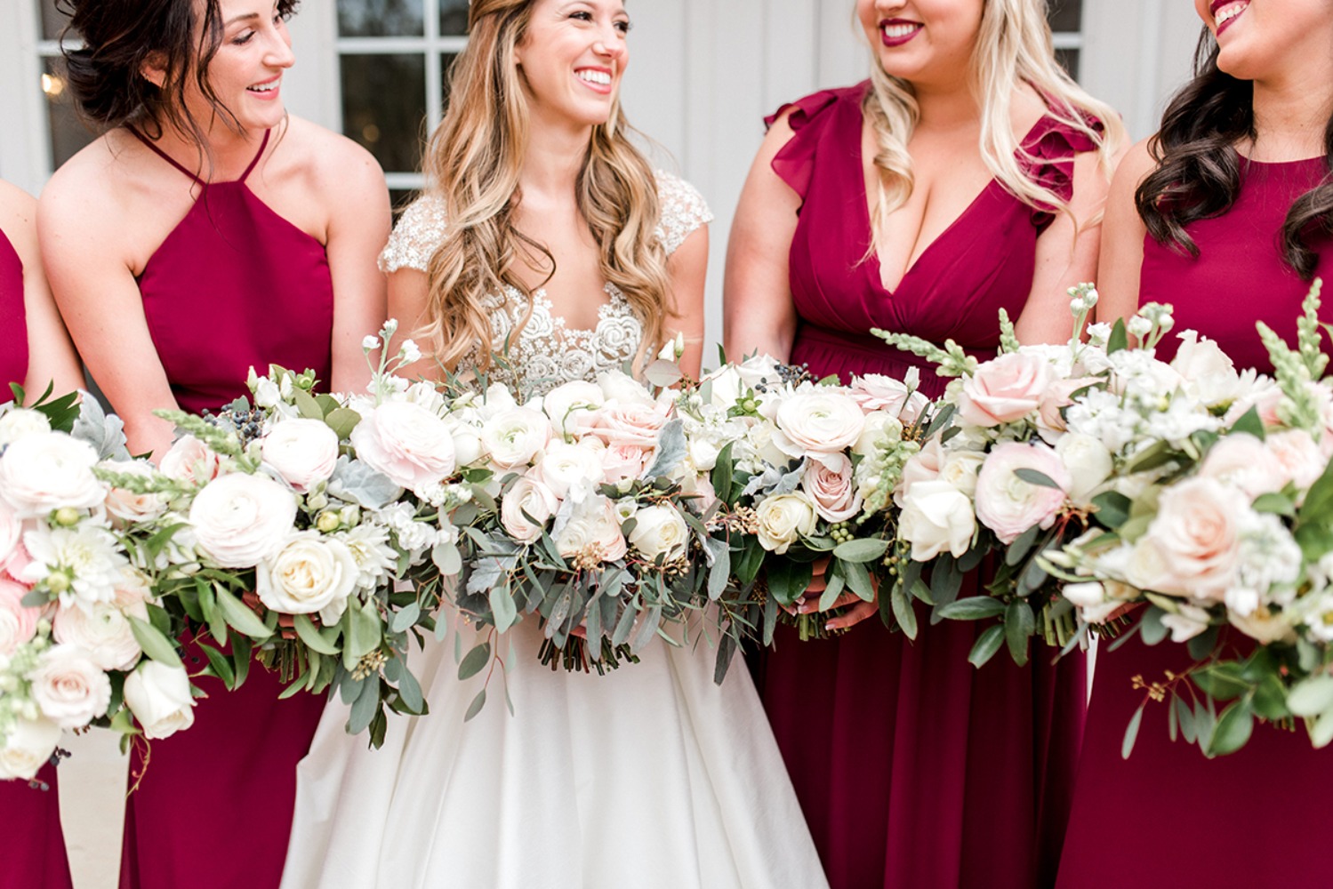 Bridesmaids smiling, holding bouquets, wearing burgundy dresses