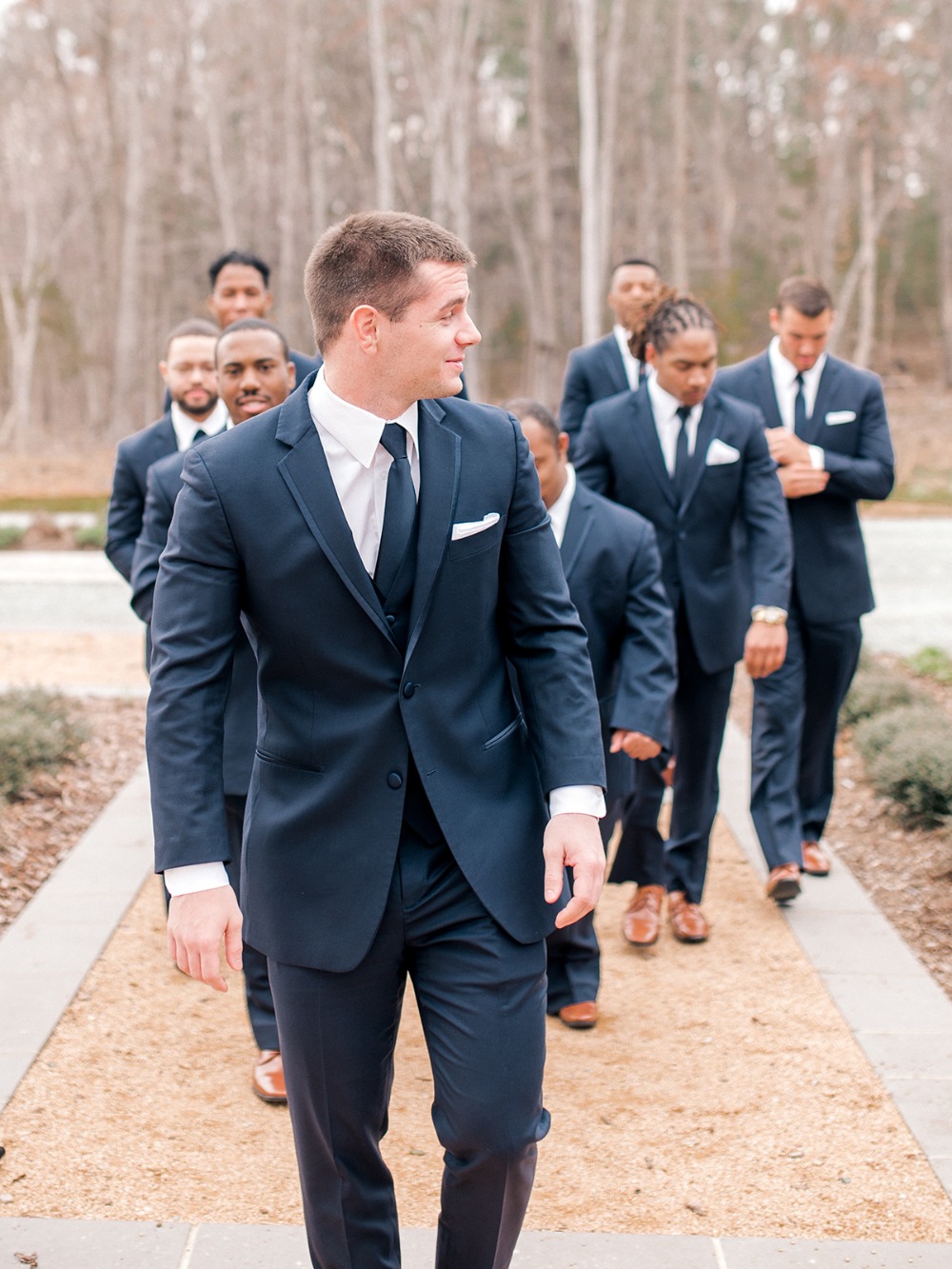 Groom and groomsmen in elegant navy suits walking together outdoors