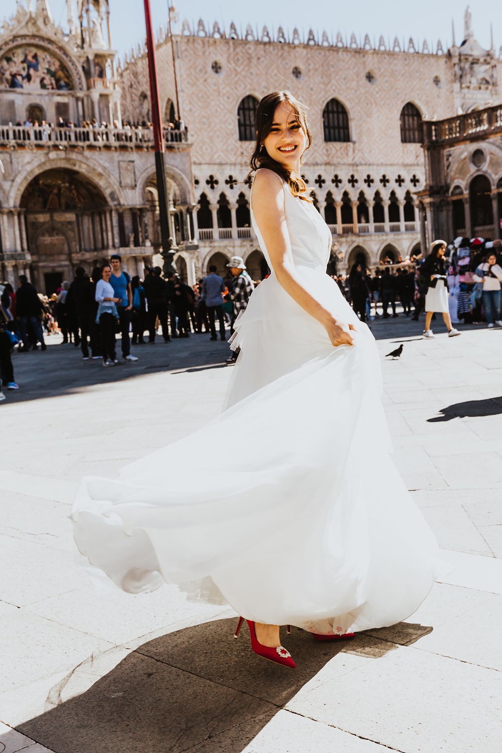 Bride twirling in a white dress with red shoes in Venice, smiling