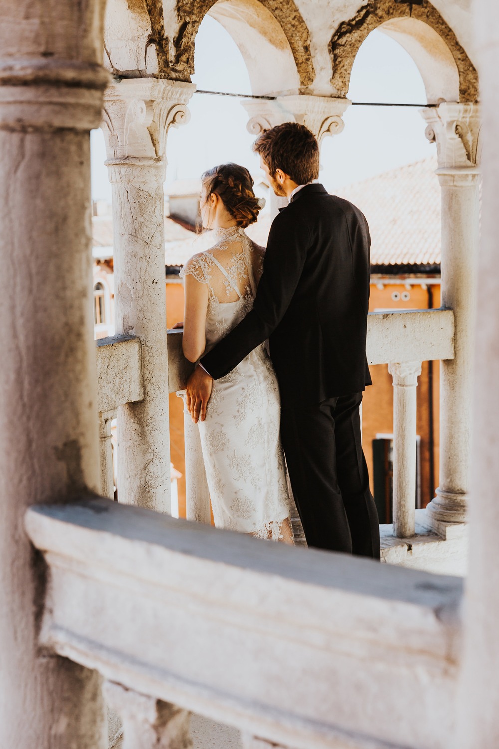 Bride and groom look out from stone balcony Venice